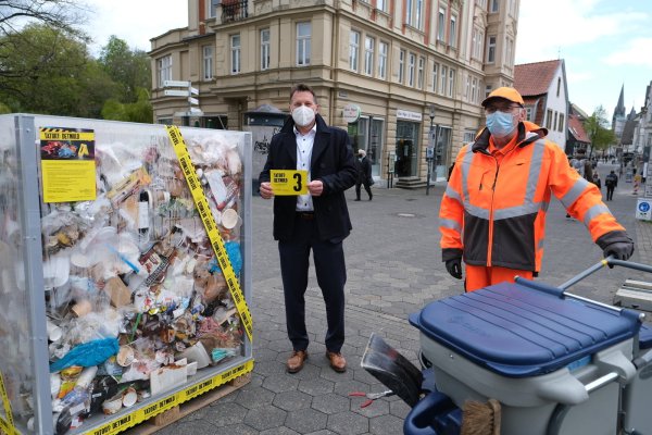 Bürgermeister Frank Hilker (links) zeigt eine der City-Cards, die mit Motto-Sprüchen bedruckt sind. Der Inhalt der Skulptur stammt aus Detmolder Straßengräben. Frank Heuman von der Stadtreinigung sammelt immer mehr Masken ein: 40 Stück pro Schicht. - © Sven Koch