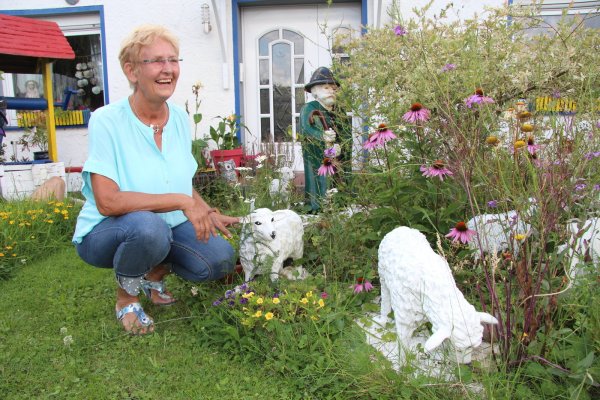 Carola Plaß sitzt „bei ihren Schäfchen“ im Garten. Dort gibt es noch viele weitere Figuren zu sehen, teilweise hat sie diese sogar selbst gestaltet. - © Nadine Uphoff