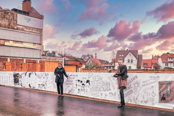 Dörte Pieper, Fachbereichsleiterin Kultur, Tourismus, Marketing und Bildungseinrichtungen bei der Stadt Detmold (links) und die Illustratorin und Designerin Nicole Sprekelmann vor dem verschönerten Bauzaun. - © Stadt Detmold