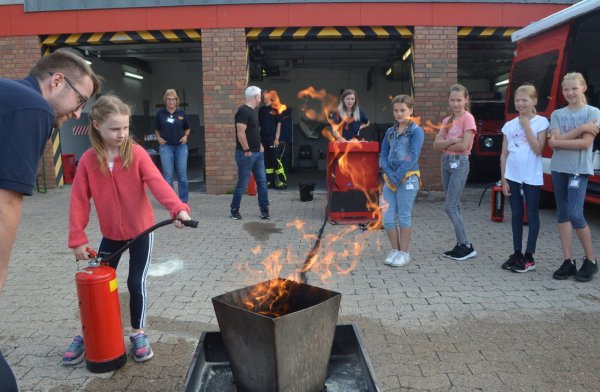 Emma löscht unter Anleitung von Patrick Althof das Feuer in der Schale, die anderen Kinder der Ferienspiel-Aktion bei der Feuerwehr schauen zu. - © Sibylle Kemna