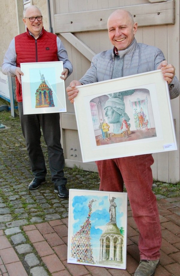 Die Geschäftsführer der Denkmal-Stiftung, Ralf Noske (vorne) und Peter Gröne, mit einigen der Karikaturen aus dem Wettbewerb „Herman the German" von 2000, die nun aus Anlass des zehnjährigen Bestehens der Stiftung ein weiteres Mal als Wanderausstellung gezeigt werden sollen. - © Barbara Luetgebrune