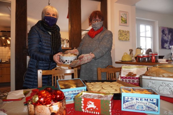 Barbara Behrens (links) überreicht Regina Zelms ihre frisch gebackenen Plätzchen. Sie freut sich schon auf die bunte Mischung an Keksen, die sie dafür zurück bekommt. - © Michaela Weiße