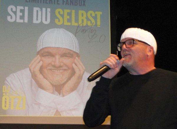 Gerry Friedle alias DJ Ötzi vor der großen Projektionswand im Kurtheater. „Sei du selbst" lautet das Motto seiner neuen CD. Rund 200 Fans nehmen ihm begeistert eine Lebensbeichte ab. - © Hajo Gärtner