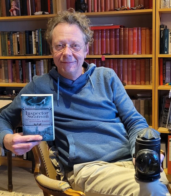 Gerald Hill alias Robert C. Marley hält seinen neuen Krimi in der Hand. In der anderen hält er eine Original-Lampe, die Polizisten im viktorianischen London in Gebrauch hatten. - © Raffael Giebel