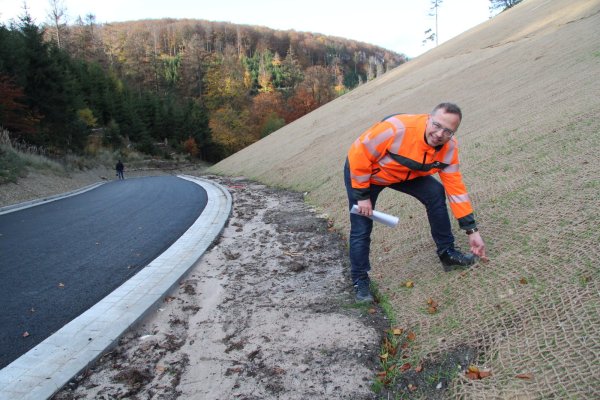 Tobias Fischer vom Landesbetrieb Straßen.NRW zupft am Sisal-Netz, das bis fast zur Kuppe des Hügels reicht. Es stabilisiert die abgeflachte Böschung und schützt die sprießenden Gräser. - © Dieter Asbrock