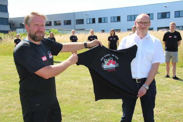 Schulsozialarbeiter Paul Oehlschläger (links) organisiert die Lauf-AG und hält mit KEB-Ausbildungsleiter Thomas Lalk die T-Shirtsspende. Über die Shirts freuen sich (von rechts) Patrick, Jesko, Tim, Lucy, Nele, Sarah, Pia, Lea, Annika. - © Seda Hagemann