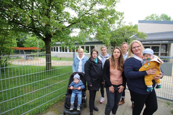 Julia Althoff mit Luca (2, v.l.), Jessica Rabe, Rebecca Gruhn, Janine Barth, Benjamin Borm und Janina Dierkes mit Henry (4) stehen vor dem Zaun der Kita. Im Hintergrund ist der Bereich für Kinder unter drei Jahren zu sehen. - © Sylvia Tetmeyer