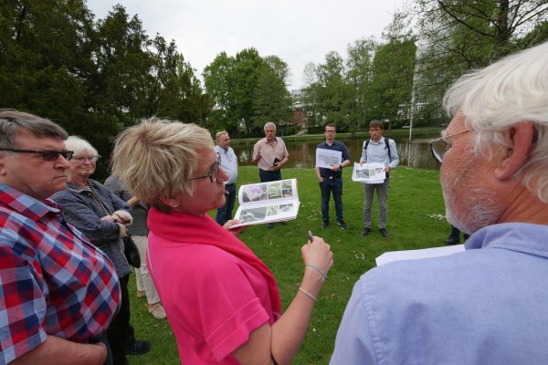 Im Mai 2022 erklärt Diana Vorndamme, Vorsitzende des Bad Meinberg e.V., während eines Rundgangs die Funktionsweise der Fitnessgeräte, die am Bad Meinberger Kurparksee platziert werden sollen. Im Hintergrund stehen (von links, mit Ausdrucken) Stadt-Pressesprecher Sebastian Vogt und Landschaftsschaftsarchitekt Matthäus Janczyk. - © Archivfoto: Jost Wolf