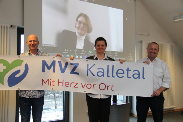 Die neuen Ärzte für Kalletal Frank Norrenbrock (von links) und Imola Kalló halten zusammen mit Bürgermeister Mario Hecker ein Banner mit dem Logo des MVZ. Im Hintergrund ist Geschäftsführerin Gabriele Dostal zu sehen, die online zugeschaltet ist. - © Nadine Uphoff