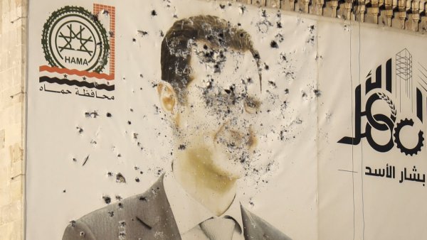 Ein Bild des ehemaligen syrischen Präsidenten Baschar al-Assad, durchlöchert von Kugeln, ist auf der Fassade des Büros der Provinzregierung nach der Übernahme der Stadt Hama durch die Opposition zu sehen. - © Omar Albam/AP