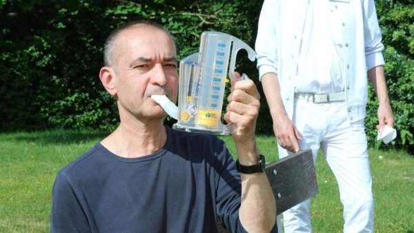 Detlef Dressler sitzt im Garten der Klinik am Burggraben und übt an seinem Atmungs-Trainingsgerät. Chefarzt Dr. Stefan Schüth beobachtet ihn mit dem nötigen Abstand. - © Alexandra Schaller