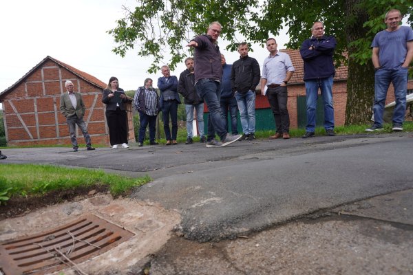 Gregor Günnewich, Fachbereichsleiter für Stadtentwicklung, Planen und Bauen, zeigt den Mitgliedern des Ausschusses, wie die so genannte Asphaltwulst das Wasser in den Kanal lenkt. - © Michaela Weiße