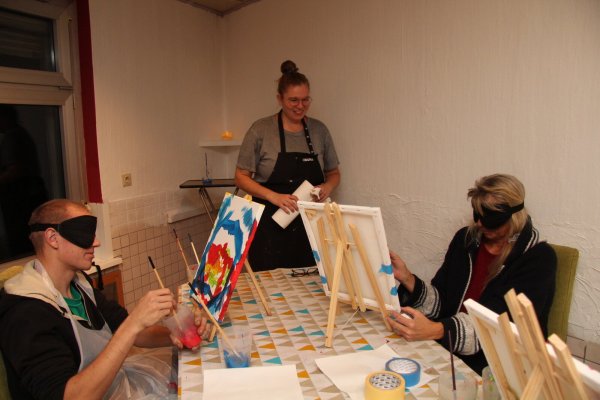 Kasimir Eckhardt und Marion malen, während sie eine Schlafmaske auf den Augen haben. Leiterin Katharina Wiesner hält Küchenrolle bereit, falls die Kursteilnehmer sich bekleckern. - © Nadine Uphoff
