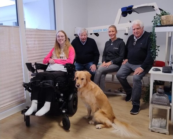 Jana Schrautemeier und ihr Assistenzhund Lio freuen sich über die Spende vom Verein Hövelstein. Hermann Josef Hüser und Reinhard Berenbrinker (Hövelstein) sowie ihre Physiotherapeutin Sabrina Sens haben sie in ihrer Wohnung in Bielefeld besucht. - © Hövelstein
