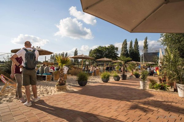 Der „Salina Beach" an der Diskothek „Glashaus" am Begakamp. Die Gäste sitzen auf Strandbänken im Sand. Rechts im Hintergrund ist die große LED-Wand zu sehen.  - © Glashaus