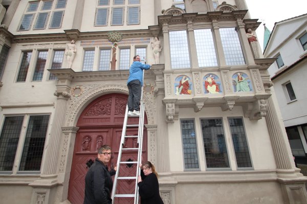 Museumsleiter Fabian Schröder misst die Eva-Figur an der Front des Hexenbürgermeisterhauses, Hausmeister Stephan Schäfsmeier und Museumsaufsicht Maike Reichert halten die Leiter. Fragen wie die nach der Figurengröße werden beim "Kultur-Quiz" am Freitag, 4. Oktober, gestellt. - © Jens Rademacher