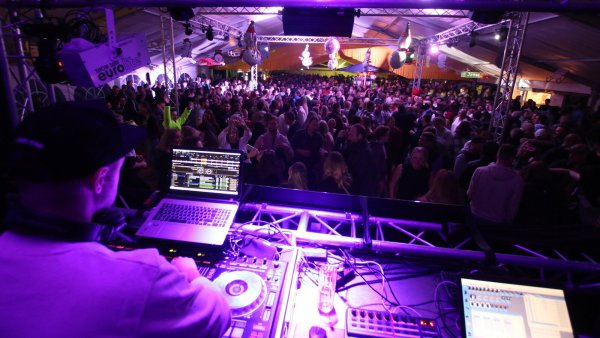 DJ Marcel Welgen hat von seinen Mischpulten aus das in buntes Disko-Licht eingehüllte und proppevolle Festzelt bestens im Blick. Unter der Decke hängen passend Deko-Schlitten und Schneemänner. Foto: Schützengesellschaft - © Schützengesellschaft