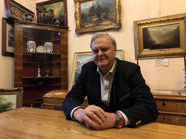 Michael Rosteck sitzt an einem alten Holztisch in einem der Verkaufsräume. Rechts hinter ihm hängt ein Motiv von Caspar David Friedrich. Das sei aber unverkäuflich, betont der Lemgoer. - © Sven Kienscherf