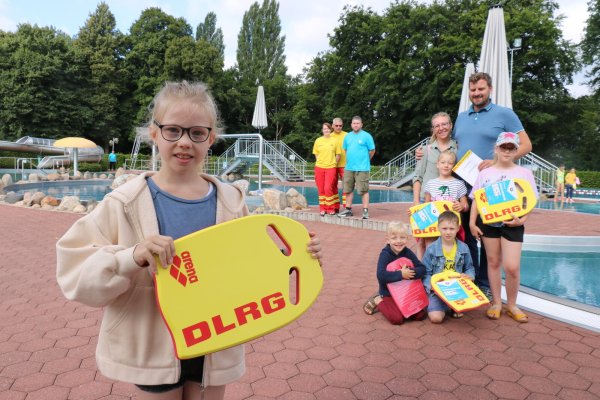 Amelie (10, vorne) hält das Schwimmbrett der DLRG, dahinter ihre Familie mit den Eltern Markus und Anna Peter sowie den Kindern (von links) Simon (5), Lynus (8), Marlene (7) und Luise (9). Dahinter stehen (von links) Bianca Wehmann und Klaus Steinkamp von der DLRG Ortsgruppe Bad Salzuflen sowie Marco Schubert, stellvertretender Bäderbetriebsleiter der Stadtwerke. - © Alexandra Schaller