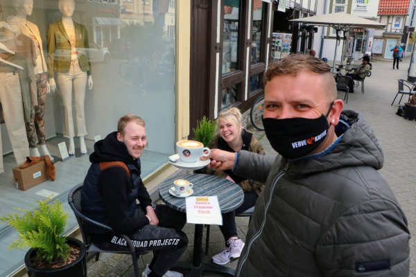 Marcel Gaus und Kim Eileen Pawliczek bestellen ihren Kaffee zu einem zusätzlichen Tisch vor der Boutique Dux Mode, der dort fürs Foto hingestellt wurde. Juri Helm vom „Café Verve" bedient. - © Yvonne Glandien
