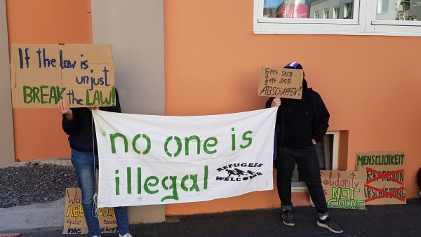 Protest auf der anderen Straßenseite: Unterstützer prangern die Flüchtlingspolitik an, gegen die sich auch der Angeklagte in seiner Aktion gewandt hatte. - © Marianne Schwarzer(LZ)