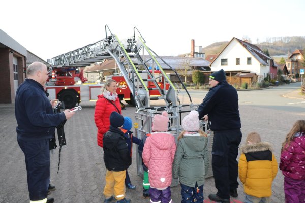 Dirk Köchling (links) und Maik Paskarbeit von der Feuerwehr Lügde haben die große Leiter ausgefahren und den Kindern und Erzieherin Christina Schaper gezeigt, wie die Feuerwehrleute in großer Höhe arbeiten und Menschen in einer speziellen Trage über die Leiter retten können. - © Johanniter Lippe-Höxter
