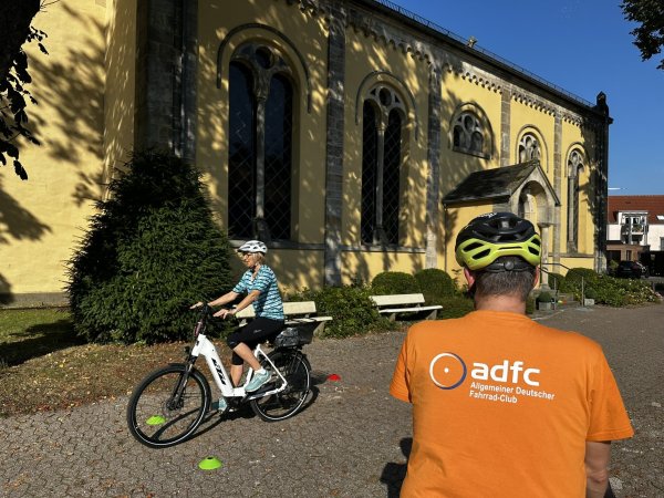 Teilnehmerin Karin Wenzel fährt unter den aufmerksamen Blicken von Trainer Lars Danzenbächer auf dem Parkour rund um die ev. Kirche in Schlangen. - © Gemeinde Schlangen