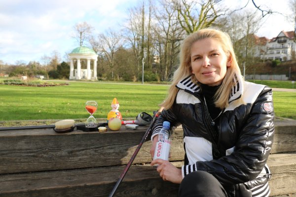 Iris Ückermann sitzt im Kurpark. Sie hat einige ihrer Utensilien mitgebracht, die sie bei ihrem Kneipp-Coaching einsetzt, um das Ganze besser zu veranschaulichen: Darunter eine Sanduhr, ein Stehauf-Männchen und Wasser. - © Alexandra Schaller