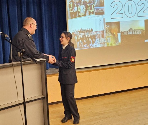 Der Leiter der Feuerwehr Lage, Benjamin Brinkmeyer, gratuliert Amelia Heel, die am Tag der Jahreshauptversammlung ihren 15. Geburtstag feierte und es sich nicht nehmen ließ, mit dem Spielmannszug in der Aula am Werreanger aufzutreten. - © Astrid Sewing