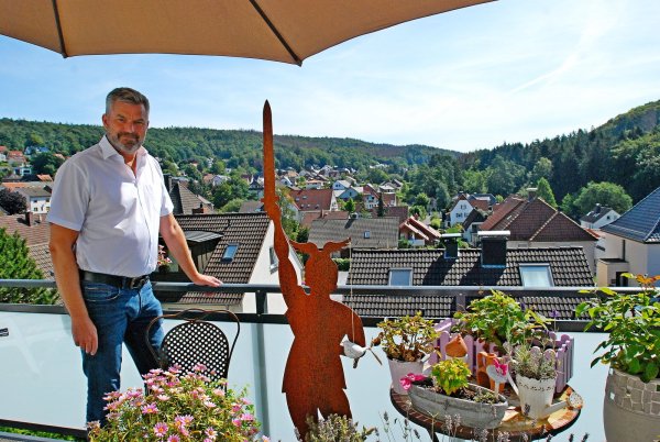 Dirk Becker im Sommer auf der Balkonterrasse seines Hauses. Neben ihm steht eine Hermann-Skulptur, der Blick geht über Oerlinghausens Häuser bis zu den Ausläufern des Teutoburger Waldes. - © Archivfoto: Gunter Held