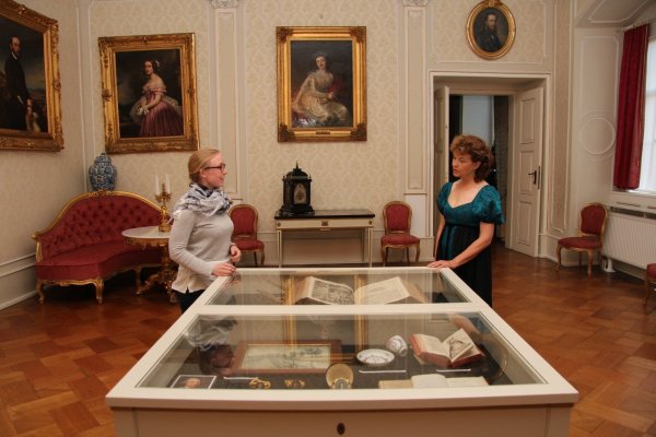 Auf ihrer Reise durch das heutige Detmold besucht Fürstin Pauline (rechts; dargestellt von LZ-Redakteurin Cordula Gröne) die Ausstellungsräume im Schloss und lässt sich von Kuratorin Lisa-Marie Bergann (links) erklären, mit welchen Stücken an sie erinnert wird. Das Gemälde zwischen ihnen im Hintergrund zeigt die Fürstin als junge Frau. - © Jana Beckmann