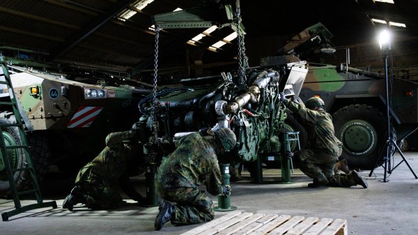 Soldaten bereiten das Anheben eines Triebwerks des gepanzerten Transportkraftfahrzeugs Boxer vor. Der mobile Kran steht in einer landwirtschaftlichen Scheune. - © Bundeswehr/Celine Liebner