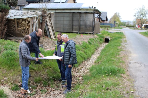 Abwasseringenieur Sven Ranft (von links), Sven Anders (Fachteamleiter Stadtentwässerung, Wasserwirtschaft), Tim Nehm (Westfalen Weser) und Beigeordneter Thorsten Paulussen schauen sich vor Ort die Pläne an. Im Hintergrund ist der Ablauf zu sehen, der nun vergrößert werden soll. Ebenso die Bodenschwelle, die versetzt wird. - © Lorraine Brinkmann