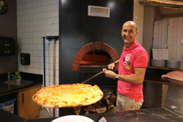Stavros Siskas mit einer frisch gebackenen Pizza aus dem Steinofen im Hintergrund. - © Alexandra Schaller