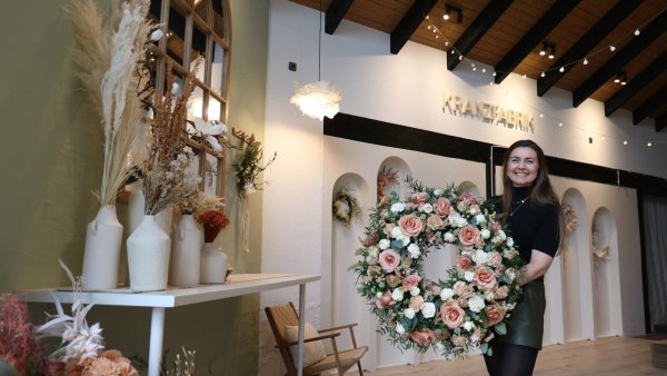 Katharina Warkentin steht mit einem großen Blumenkranz in ihrer "Kranzfabrik". - © Alexandra Schaller