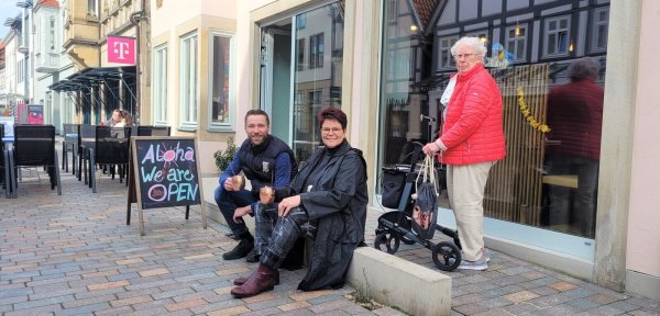 Sitzen auf dem Stein des Anstoßes: Alexander Rembold, Pächter vom Malhalo, und Hauseigentümerin Manuela Kramp. Währenddessen rollt Ilse Koslowski mit dem Rollator die Rampe hinauf und ist dankbar, dass der barrierefreie Zugang zum Restaurant für sie so übersichtlich und praktikabel ist. - © Katrin Kantelberg