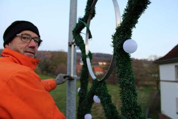 Dirk Herrmann befestigt die Sterne an den vorhandenen Haken, das Kabel wird in einer Steckdose auf der Rückseite eingesteckt. - © Lorraine Brinkmann