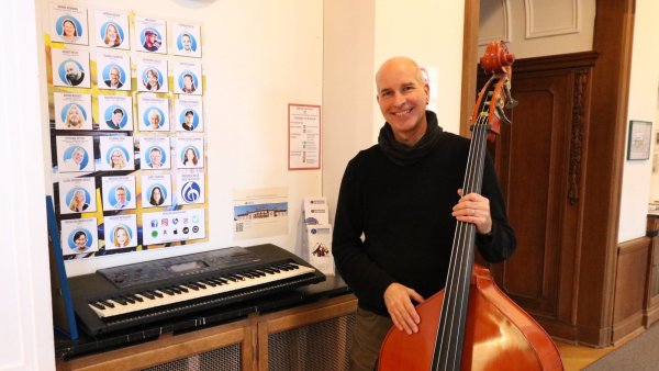Stephan Otters steht mit Kontrabass und Keyboard vor dem Plakat seines Teams - ohne sie hätte er die 25 Jahre in Bad Salzuflen so nicht gestemmt, sagt er. - © Alexandra Schaller