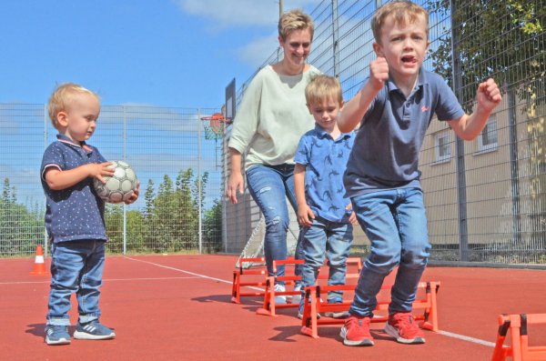 Früh übt sich: Zuschauer Liam (v.l.), Mama Nicole mit Luca (3) und Levi (5) hüpfen im Schlusssprung über kleine Hürden - eine Übung aus dem Anfängertraining der Handballer, die man auf dem Sportfest ausprobieren konnte. - © Sibylle Kemna