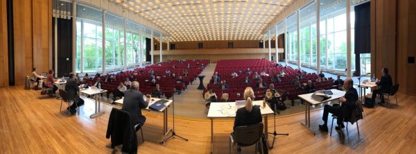 Der Rat tagt in den Weiten der Konzerthalle. Auf der Bühne hat der Verwaltungsvorstand Platz genommen. In den vorderen Reihen sitzen Ratsmitglieder. Im Hintergrund verfolgen Gäste das Geschehen. - © Thomas Reineke