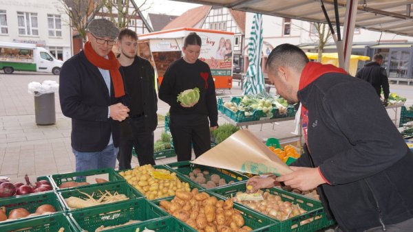 Kochmeister Arnaud Brun, Fachlehrer am Felix-Fechenbach-Berufskolleg in Detmold, kauft gemeinsam mit seinen Schülern Jason Kröker und Vivien Steinmair auf dem Blomberger Wochenmarkt die Zutaten für das Menü ein. Am Obst- und Gemüsestand von Metehan Agcan können sie sogar den Preis etwas verhandeln. - © Michaela Weiße