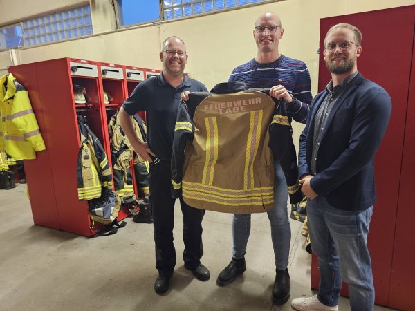 Wehrleiter Benjamin Brinkmeyer, Pressesprecher Carlos Hummerjohann und Fachgruppenleiter Malte Begemann zeigen eine Testjacke. Weil sie rundum mit Reflektorstreifen vershen ist, entfällt die Pflicht, Warnwesten zu tragen. - © Astrid Sewing