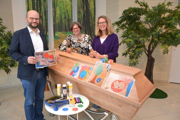David Heilmann, Brigitte Blomberg und Nina Ross (v. l.) hinter einem Sarg, der bemalt werden könnte. Einige Bilder zeigen, welche Motive Kinder gemalt haben. Foto: Karin Prignitz - © Karin Prignitz