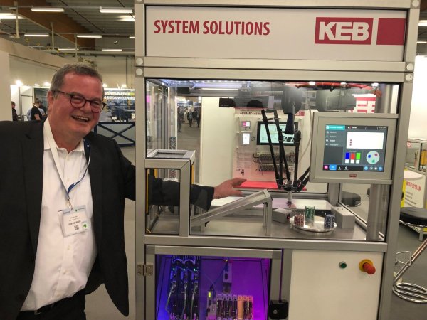 Keine Angst vor dem Roboterarm: Detlef Loest von der Firma KEB Automation (Barntrup) greift auf der Zuliefermesse Maschinenbau wortwörtlich in einen vollautomatischen Produktionsprozess ein. Der Roboterarm, der zuvor noch schwungvoll Spielchips verteilt hat, wird erst langsamer und stoppt dann gänzlich. „Gewarnt“ wird er vor der Menschenhand von zwei aufeinanderfolgenden Lichtschranken. - © Thomas Reineke
