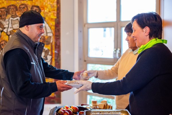 Timucin Sirin (links) nimmt einen Teller Gulaschsuppe von Judith Brazier (rechts) entgegen. Maria Tuschewitzki reicht ein Stück Brot. - © Raphael Bartling