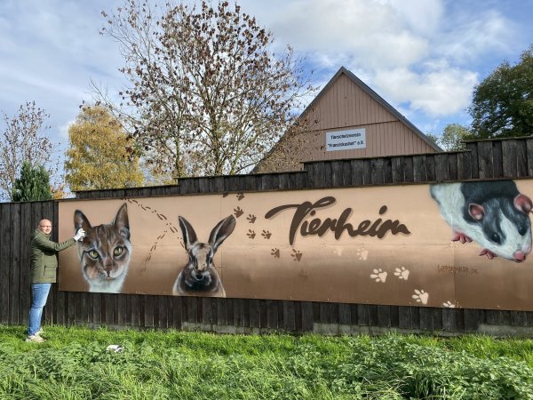 Künstler Maik Enge zeigt das Kunstwerk, das er auf dem Zaun des Franziskushofs gestaltet hat. - © Fotorechte: Tierheim Franziskushof