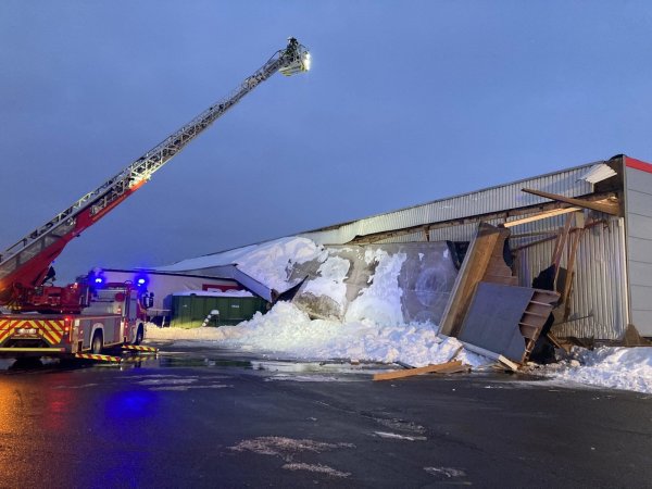 Schneemassen haben das Vordach der Produktionshalle heruntergedrückt. „Begraben" sind unter anderem zwei Lkw-Sattelauflieger. Die Holzbalken, die das Vordach stützten (wie beispielsweise rechts zu sehen), reichen in die eigentliche Halle herein und sind teilweise hochgedrückt worden.  - © Feuerwehr Bad Salzuflen
