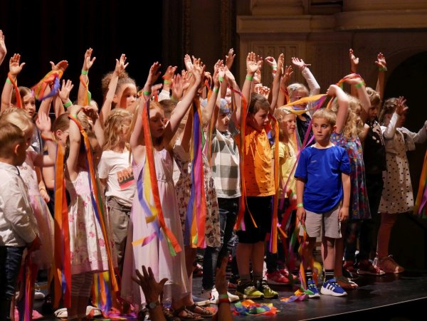 Wir sind Kinder einer Welt. Rund 80 Kinder begrüßen die Gäste mit bunten Bändern auf der Bühne im Großen Saal. - © Thomas Krügler
