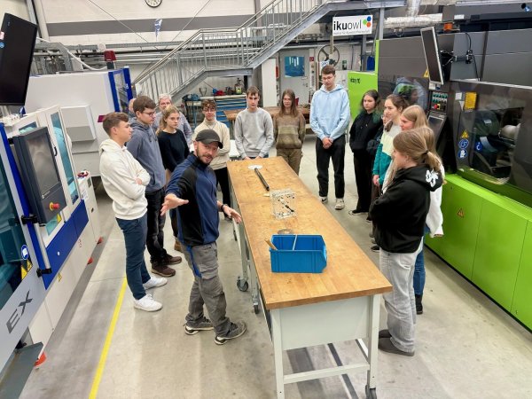 Der Kunststoffprofi Lukas Dunsche (Lippe Bildung eG) erklärt den Schülerinnen und Schülern anschaulich, wie die Spritzgussmaschine funktioniert, die direkt vor ihnen steht. - © Lippe Bildung eG