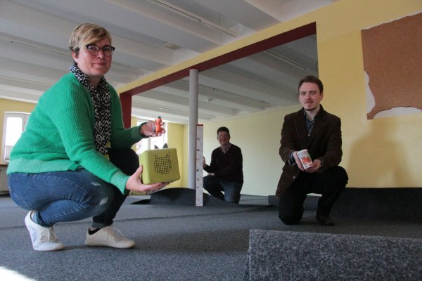Im Obergeschoss wird ein neuer Teppichboden in der Kinderbücherei verlegt. Bücherei-Mitarbeiterin Anika Beuke präsentiert hier die Toniebox mit dem Kleinen Drachen Kokosnuss. Dabei sind auch Leiter Axel Koch (Mitte) und Azubi Björn Bohnert. - © Carolin Brokmann-Förster